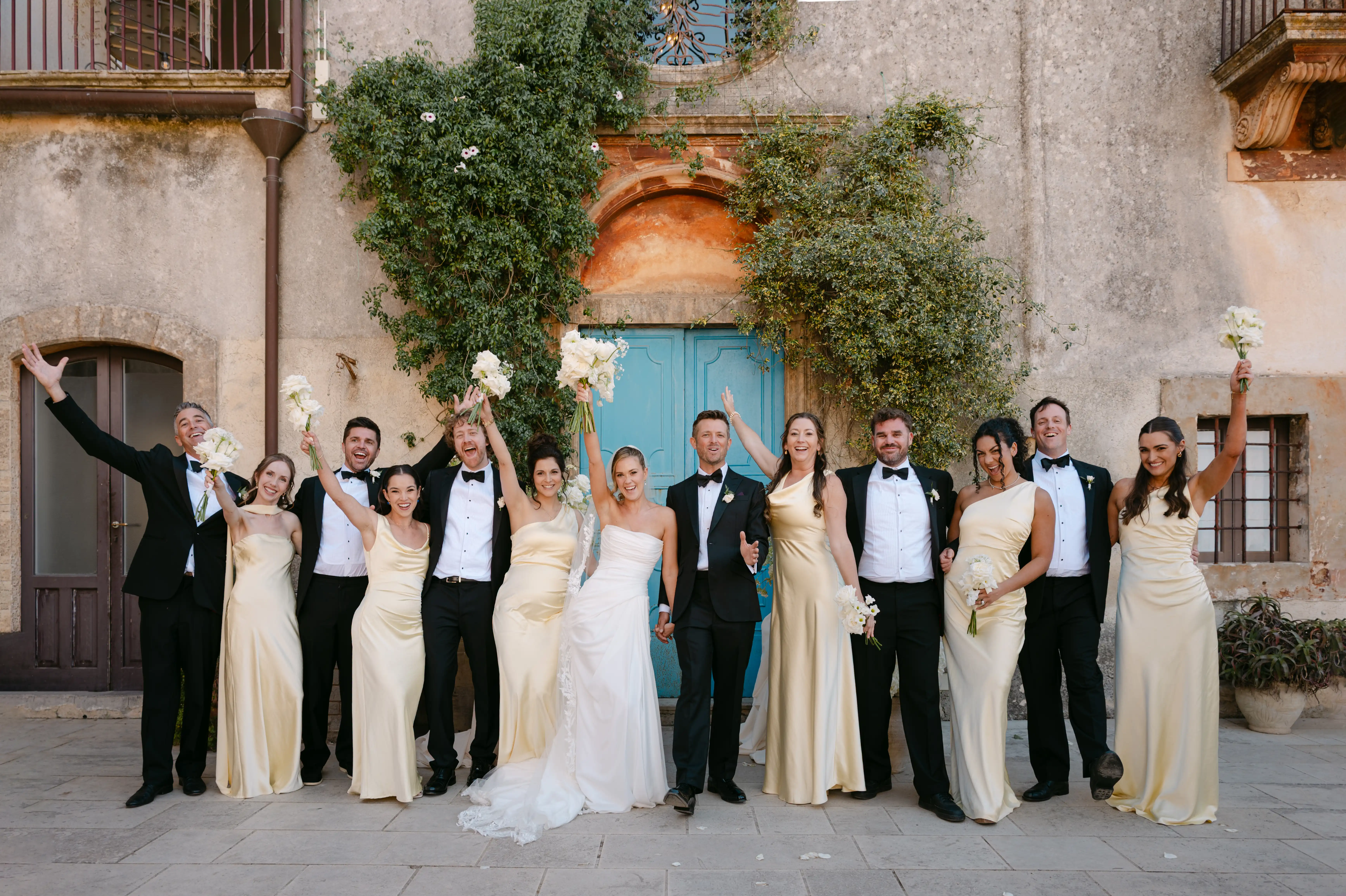 Bride and groom celebrating with bridesmaids and groomsmen in front of a rustic Italian villa.